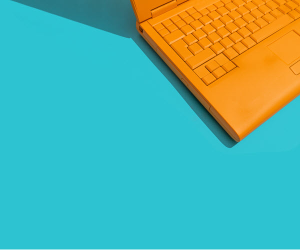 A partial view of an orange laptop's keyboard on top of a flat turquoise background.