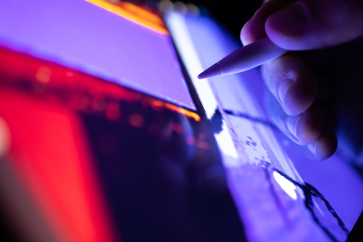 Close-up of a hand holding a stylus as it reaches toward a colorful digital display.