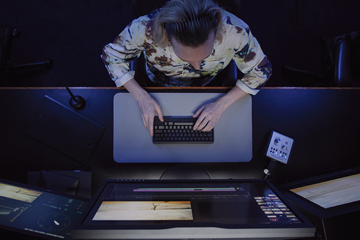 A person sits in front of multiple computer monitors while typing on a an HHKB Studio keyboard.
