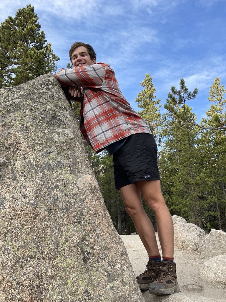 AWS Senior Solutions Architect, Michael Mumma next to a shoulder-high rock with large alpine trees in the background