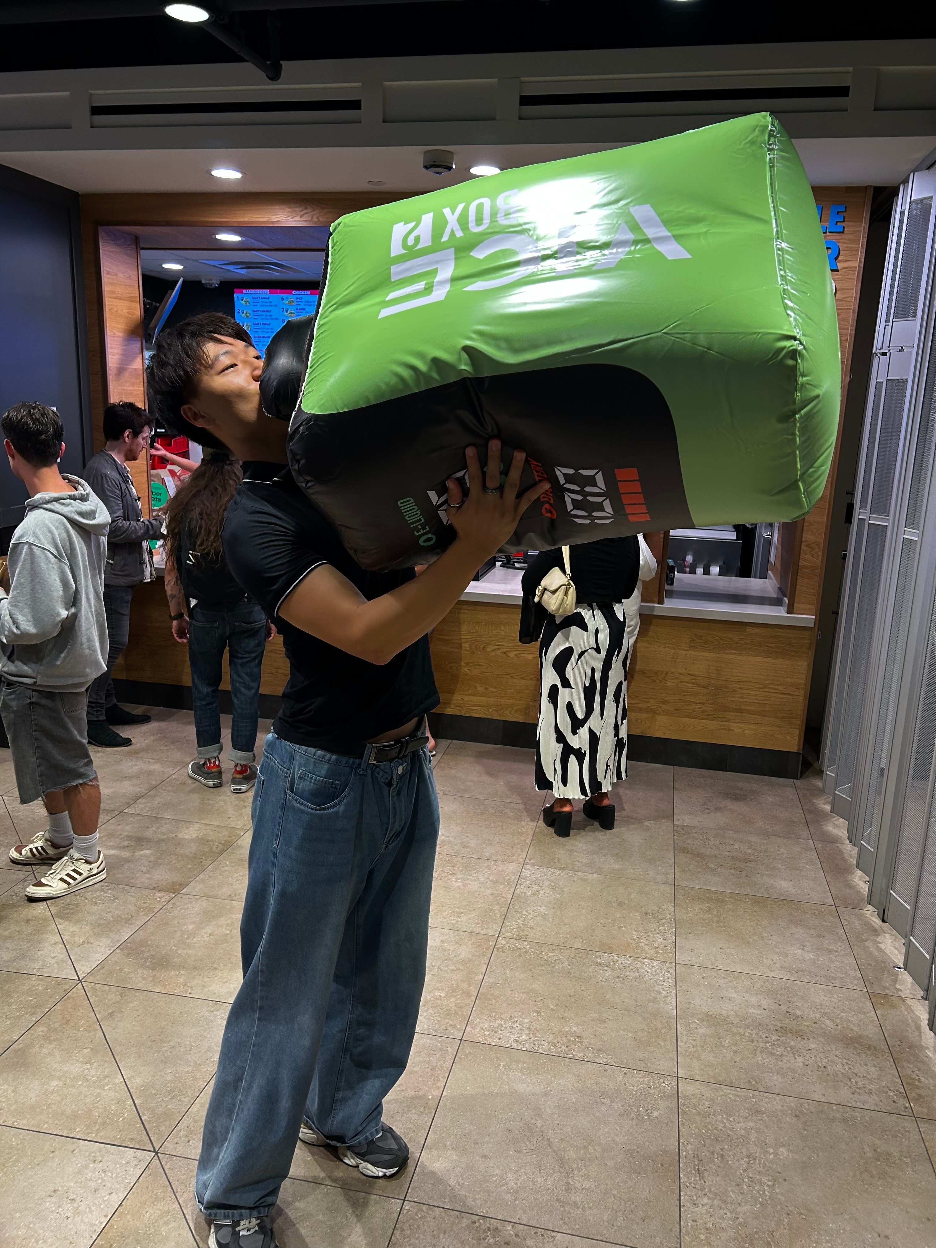 James Yang holding a large inflatable energy drink and pretending to sip from it.