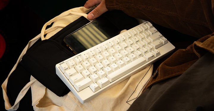 White HHKB keyboard sitting on top of a canvas bag with someone holding it. 