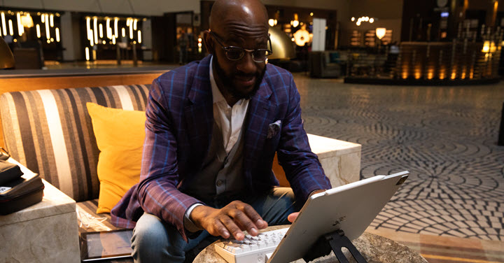 Black man sitting at a hotel lobby using a wireless keyboard and screen. 