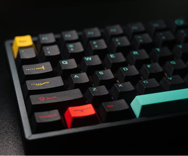 Close-up view of the left half of a mechanical keyboard, with the body of the board and keycaps in black and various accent pieces in yellow, red, and teal.