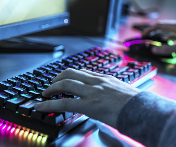 Closeup of a person using a desktop computer, focused on a keyboard with colorful RGB underlighting.