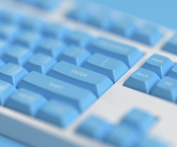 An oblique close-up of a keyboard with a white case and blue keycaps. The enter key is in focus and the rest of the board is progressively more blurry.