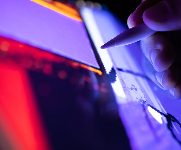 Close-up of a hand holding a stylus as it reaches toward a colorful digital display.