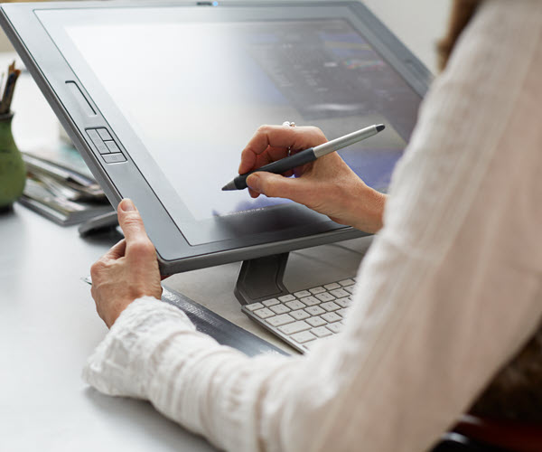 Behind-the-shoulder view of a person working on a tilted graphics tablet, with a keyboard partially visible under the tablet.
