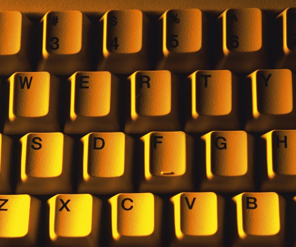 A top-down, close-up of keyboard keys light from the side with a bright orange light.