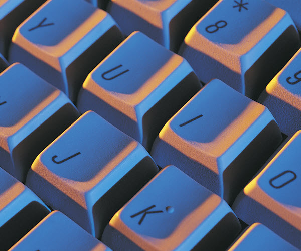 A close-up of computer keyboard keys at an oblique angle, lit by a cool light from one side and a warm light from the other.