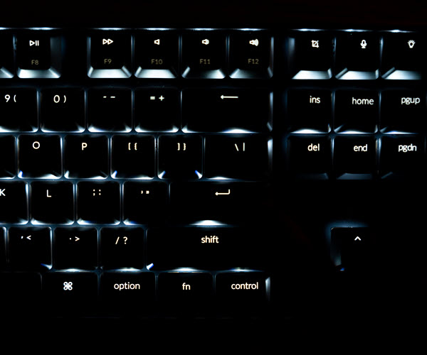 White underlighting illuminates the keys of a tenkeyless keyboard in an otherwise dark image.