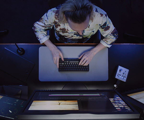 A person sits in front of multiple computer monitors while typing on a an HHKB Studio keyboard.